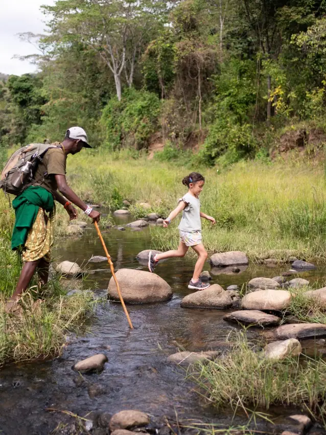 Family crossing forest stream on stepping stones, Kitich Camp, Northern Kenya, Kenya