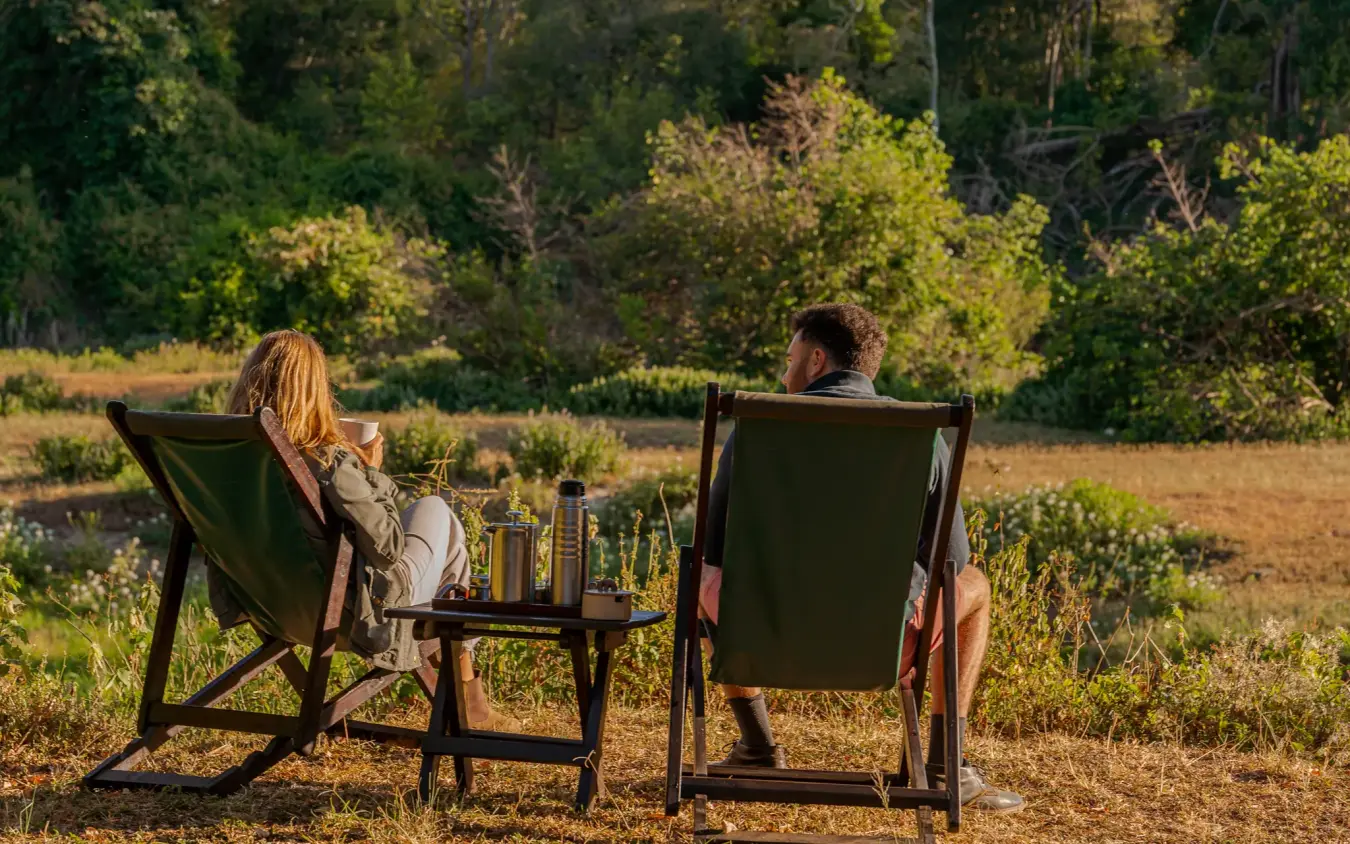Two guests relaxing in chairs overlooking forest landscape, Kitich Camp, Northern Kenya, Kenya