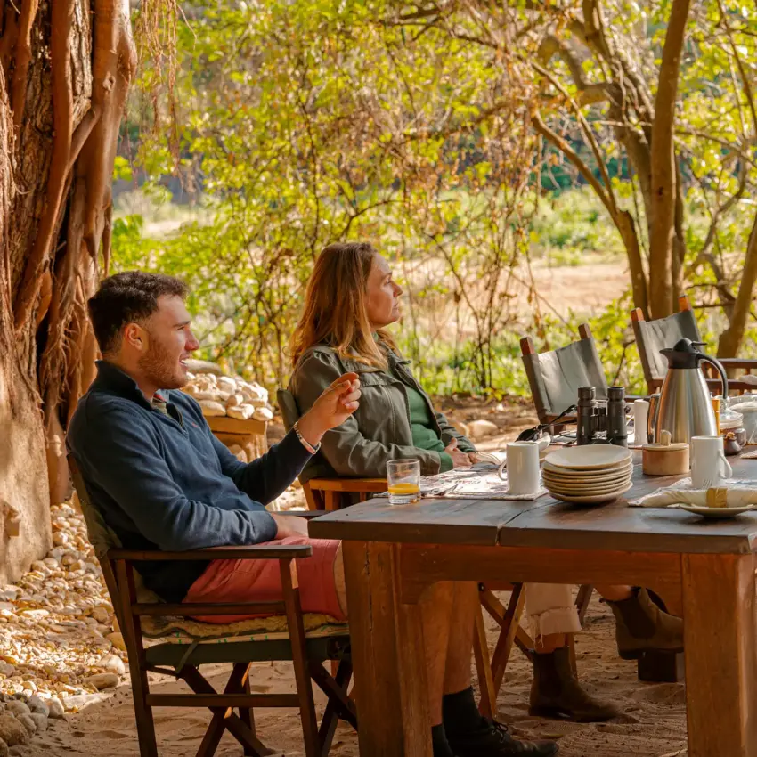 Three guests dining at outdoor table under tree canopy, Kitich Camp, Northern Kenya, Kenya