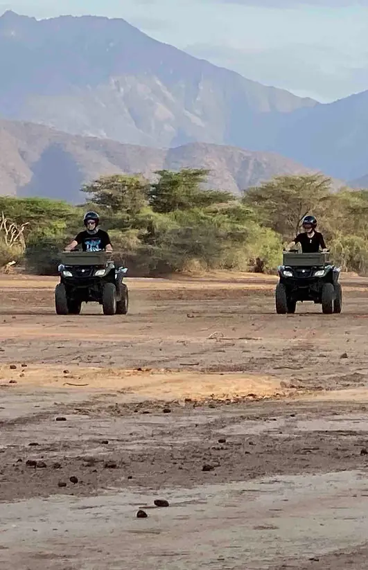 Four guests on ATVs lined up in desert landscape, Koros Camp, Northern Kenya, Kenya