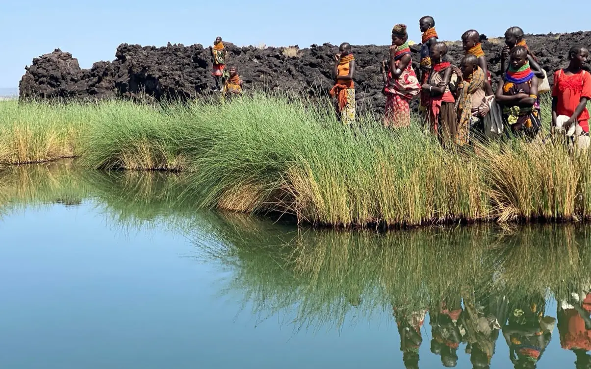 Group of people standing by water with lush vegetation, Koros Camp, Northern Kenya, Kenya
