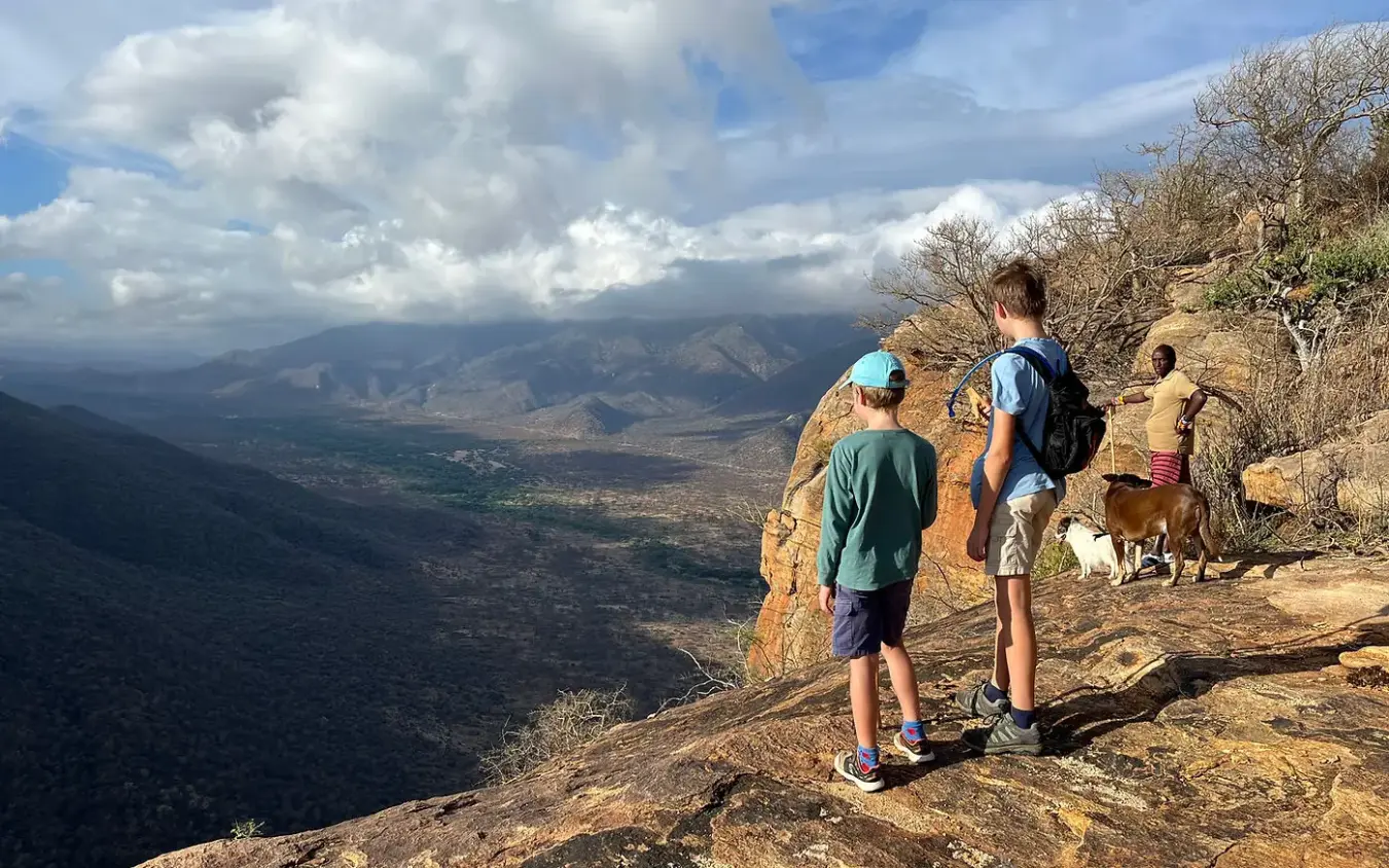 Hikers standing on rocky outcrop overlooking valley, Koros Camp, Northern Kenya, Kenya
