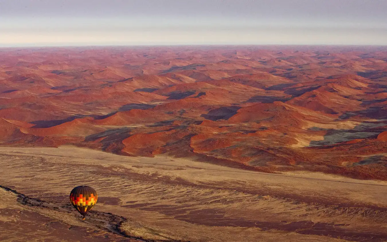 Hot air balloon floating over vast desert landscape at sunrise, Kulala Desert Lodge, Sossusvlei, Namibia