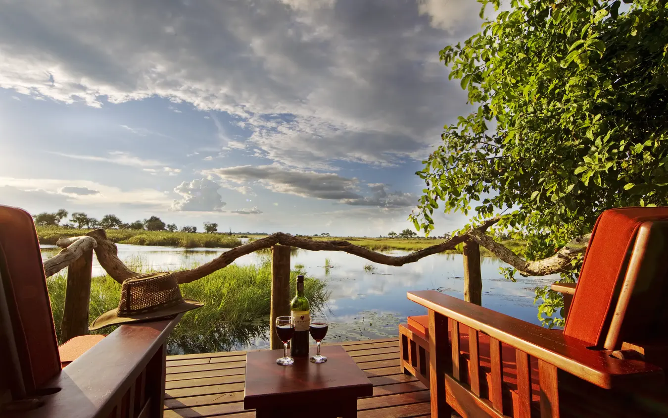 Wooden deck with wine glasses overlooking wetland and floodplain at dusk, Kwando Lagoon Camp, Linyanti Wildlife Reserve, Botswana