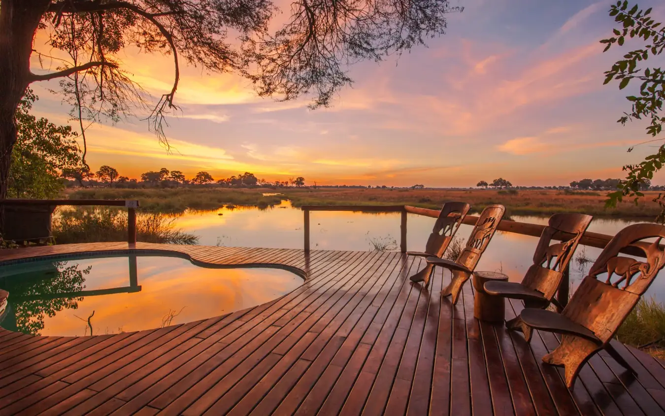 Wooden deck with chairs overlooking floodlit waterhole at sunset, Kwando Lagoon Camp, Linyanti Wildlife Reserve, Botswana