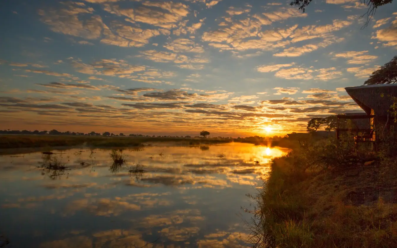 Sunrise reflecting in floodwaters with lodge overlooking wetland, Kwando Lagoon Camp, Linyanti Wildlife Reserve, Botswana