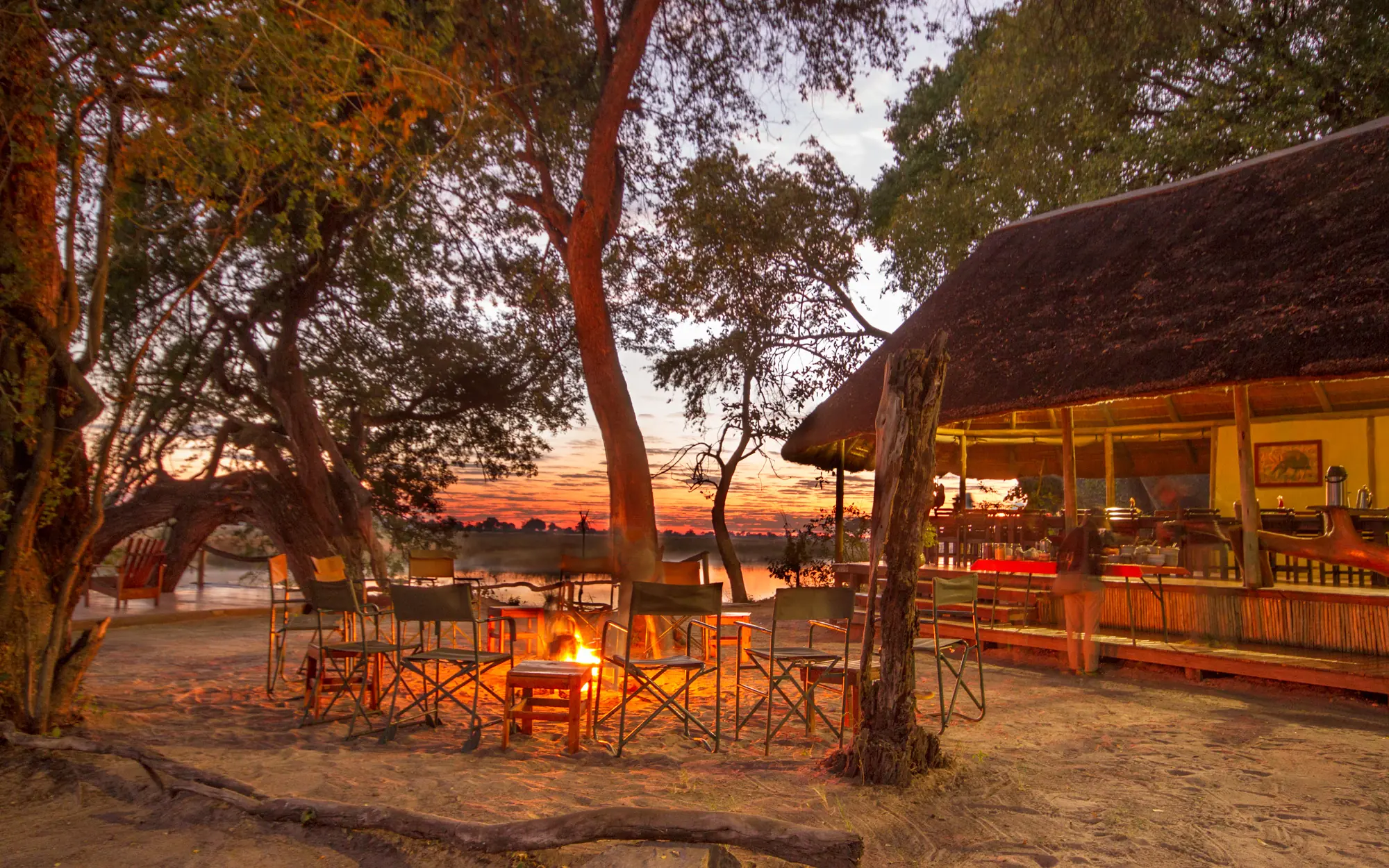 Beachfront camp lounge with firepit at sunset overlooking waterfront, Kwando Lagoon Camp, Linyanti Wildlife Reserve, Botswana