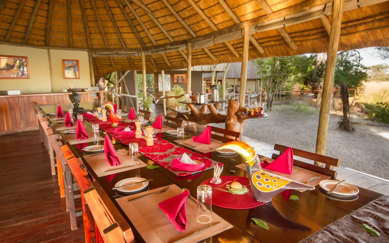 Open-air dining pavilion with red napkins and wooden tables under thatched roof, Kwando Lagoon Camp, Linyanti Wildlife Reserve, Botswana