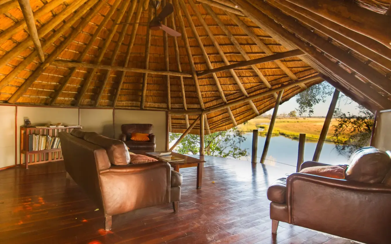 Thatched lodge interior with leather seating overlooking waterfront savanna, Kwando Lagoon Camp, Linyanti Wildlife Reserve, Botswana