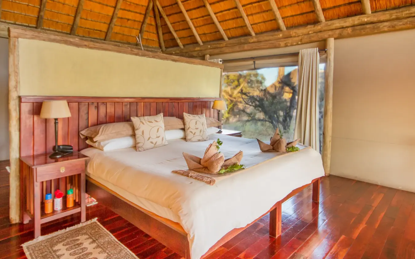 Luxury safari bedroom with wooden furnishings overlooking acacia trees, Kwando Lagoon Camp, Linyanti Wildlife Reserve, Botswana
