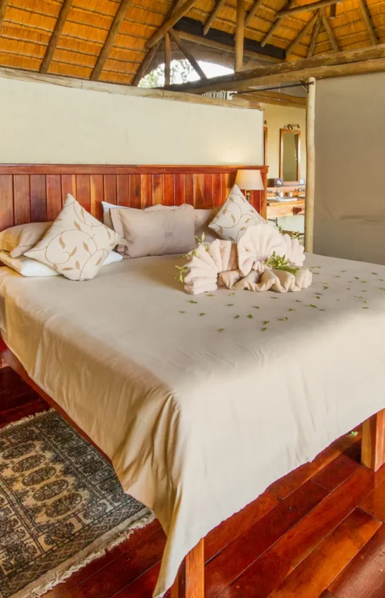 Luxury bedroom with wooden headboard and rose petals on bed, Kwando Lagoon Camp, Linyanti Wildlife Reserve, Botswana