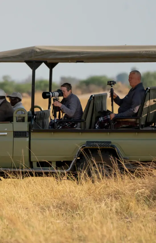 Safari vehicle with photographers on game drive in dry grassland, Kwando Lebala Camp, Linyanti Wildlife Reserve, Botswana
