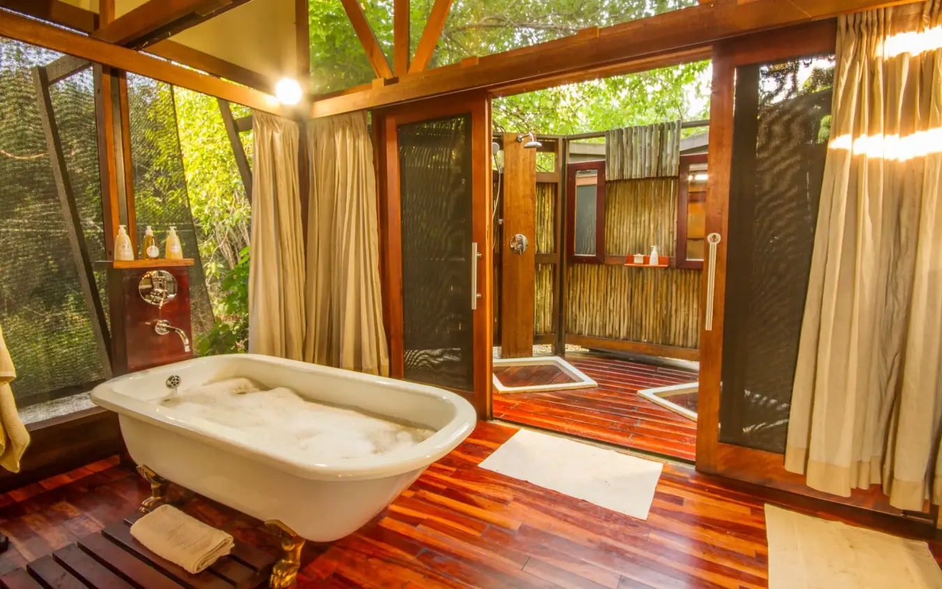 Luxury bathroom with freestanding tub and forest views through large windows, Kwando Lebala Camp, Linyanti Wildlife Reserve, Botswana