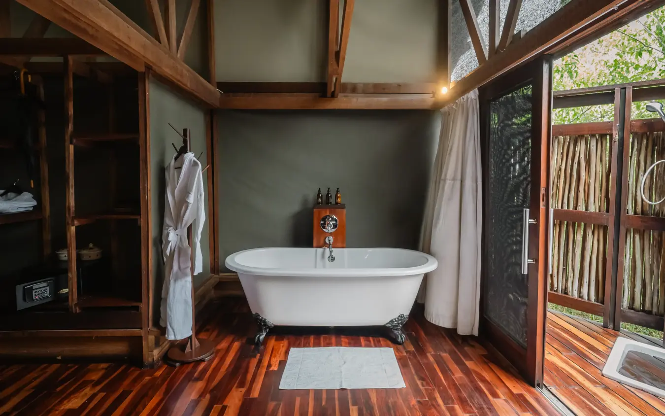 Outdoor bathroom with freestanding bathtub and wooden deck overlooking garden, Kwando Lebala Camp, Linyanti Wildlife Reserve, Botswana