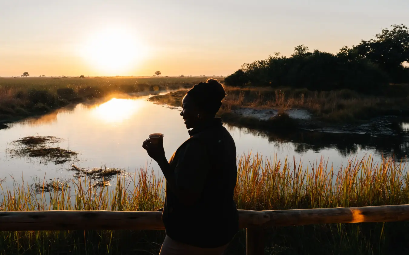 Silhouetted person with binoculars overlooking wetland at sunrise, Kwando Lebala Camp, Linyanti Wildlife Reserve, Botswana