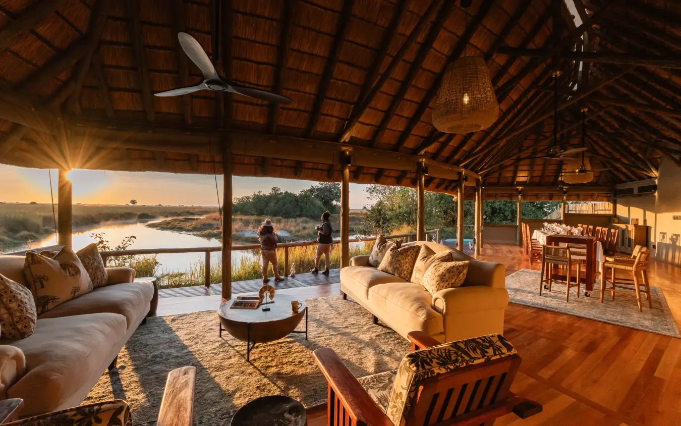 Open-sided lodge pavilion overlooking waterhole at sunset with guests gathered on deck, Kwando Lebala Camp, Linyanti Wildlife Reserve, Botswana