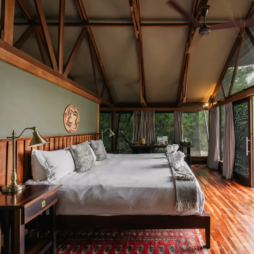 Luxury bedroom with wooden beams overlooking forest canopy from expansive windows, Kwando Lebala Camp, Linyanti Wildlife Reserve, Botswana