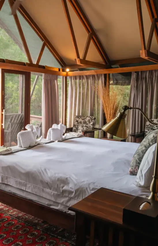 Luxury bedroom suite with wooden beams and panoramic windows overlooking woodland, Kwando Lebala Camp, Linyanti Wildlife Reserve, Botswana