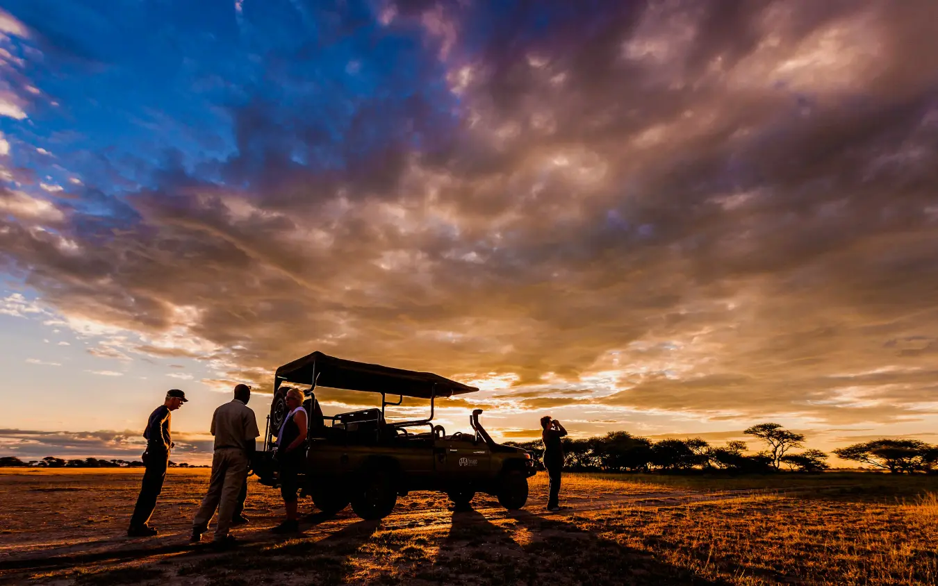 Safari vehicle and guests silhouetted at sunset in open grassland, Kwando Nxai Pan Camp, Makgadikgadi Pans, Botswana