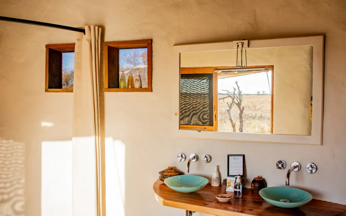 Bathroom with dual sinks and mirror overlooking arid landscape through windows, Kwando Nxai Pan Camp, Makgadikgadi Pans, Botswana