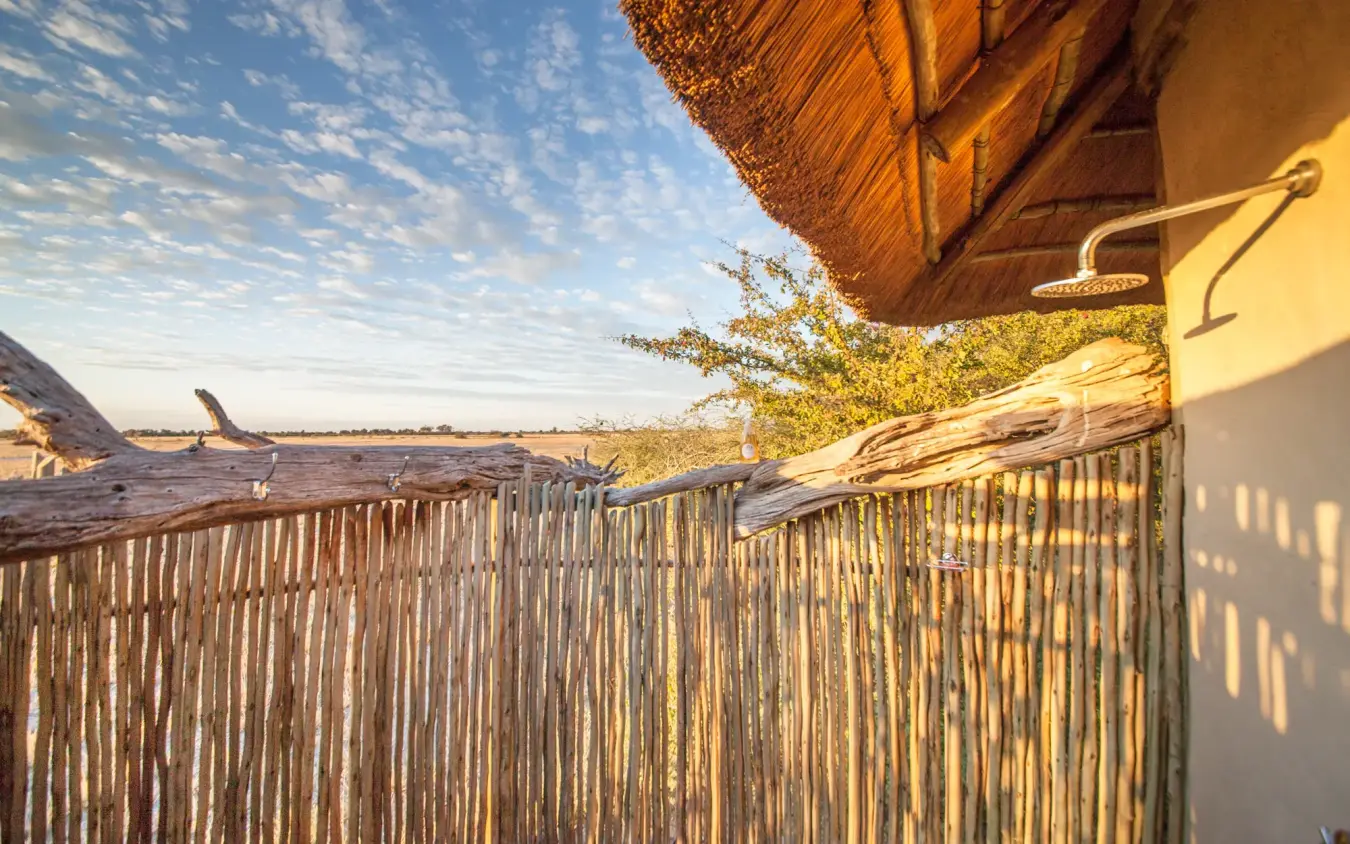 Wooden deck with thatch roof overlooking waterhole at sunset, Kwando Nxai Pan Camp, Makgadikgadi Pans, Botswana