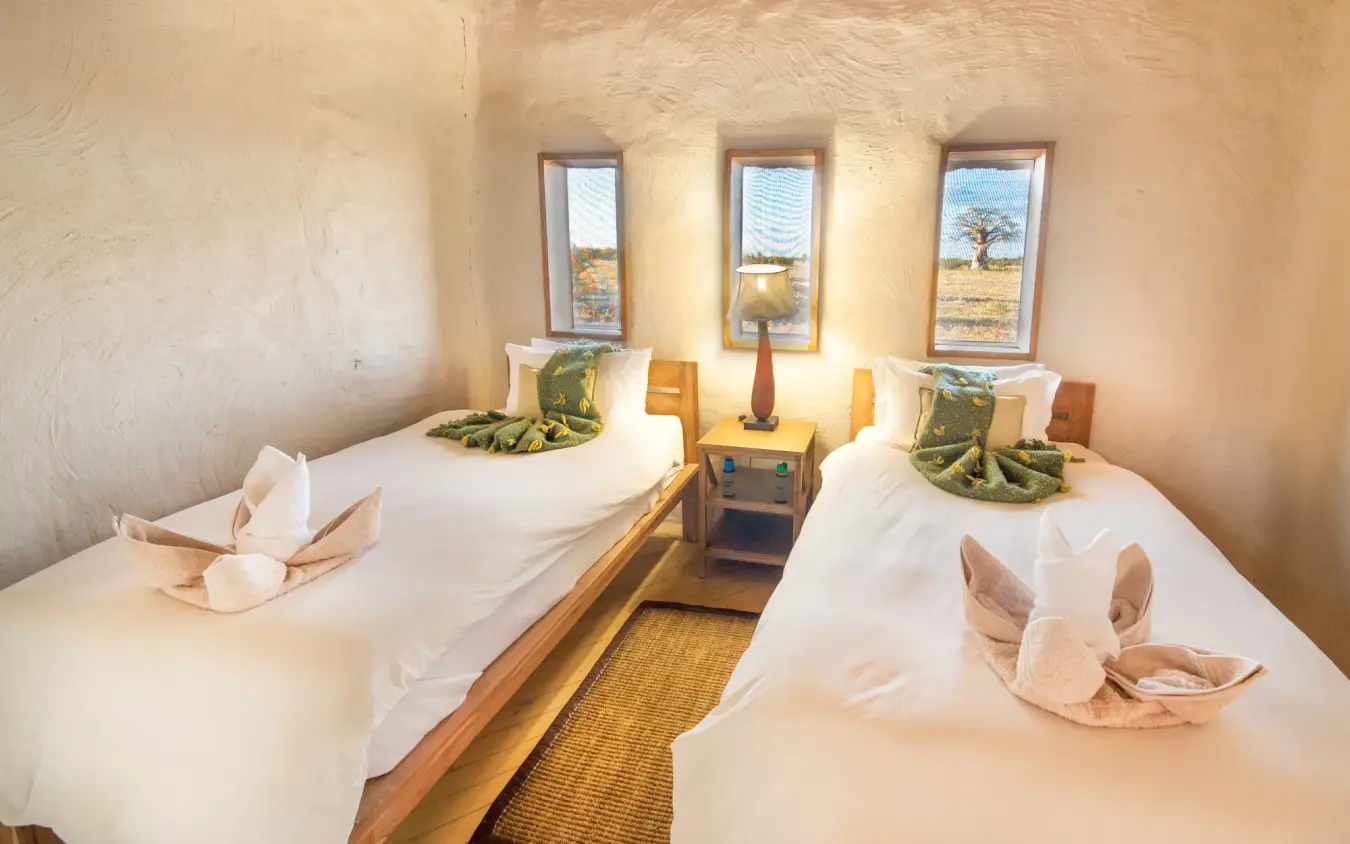Twin beds in safari lodge room with woven grass decor and valley views, Kwando Nxai Pan Camp, Makgadikgadi Pans, Botswana