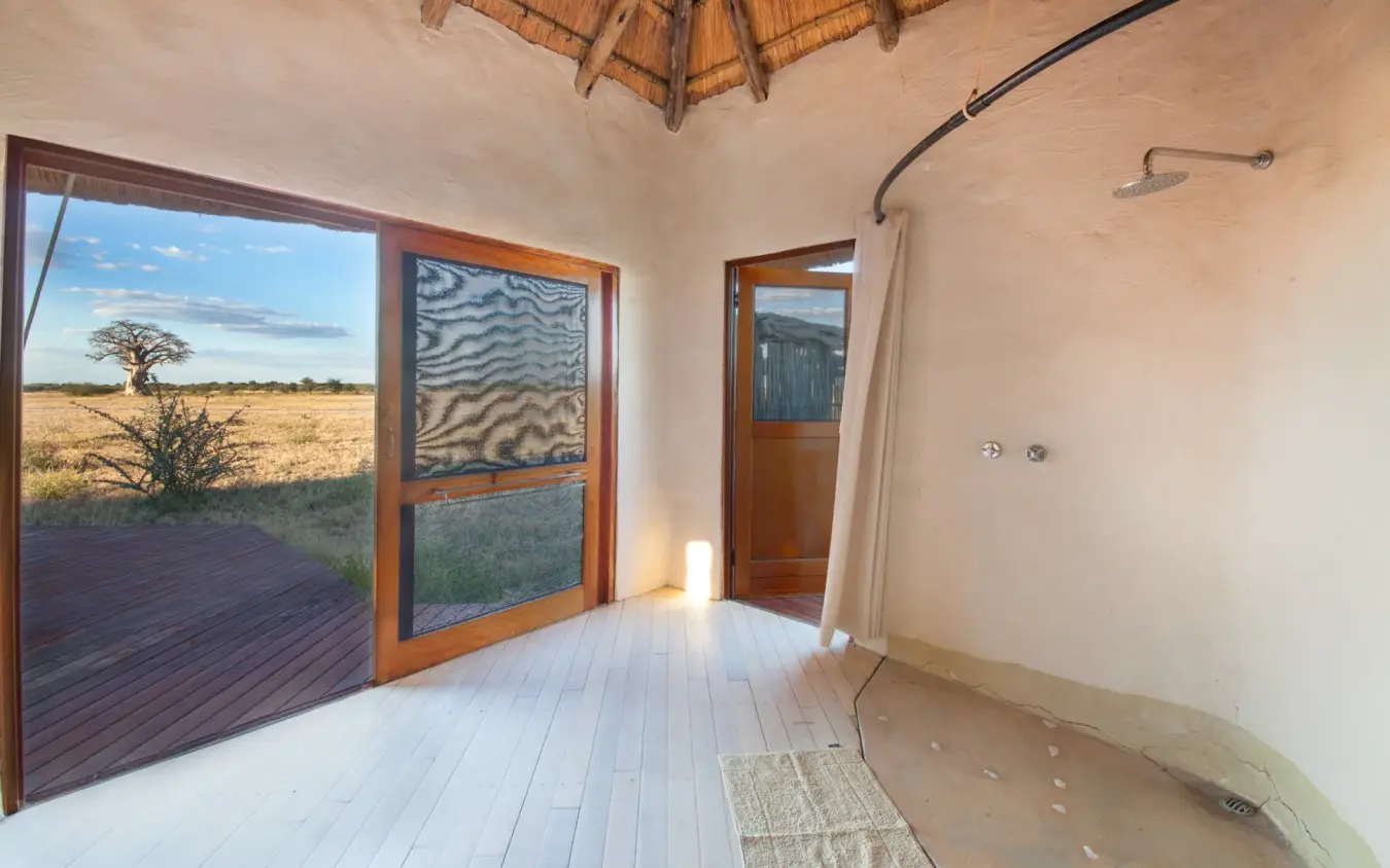 Open-air bedroom interior with savanna views through glass doors, Kwando Nxai Pan Camp, Makgadikgadi Pans, Botswana