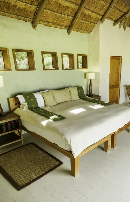 Spacious bedroom with thatched roof and views through multiple windows, Kwando Nxai Pan Camp, Makgadikgadi Pans, Botswana