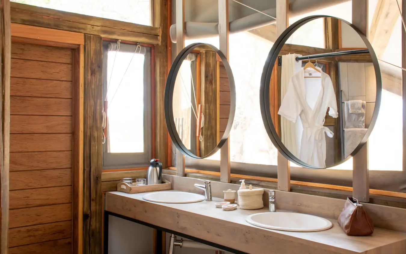 Luxury safari lodge bathroom with double vanity and round mirrors overlooking savanna, Kwando Splash Camp, The Okavango Delta, Botswana