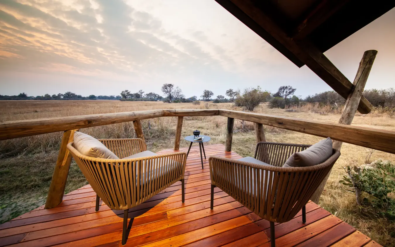 Wooden deck with woven chairs overlooking vast grassland at sunset, Kwando Splash Camp, The Okavango Delta, Botswana