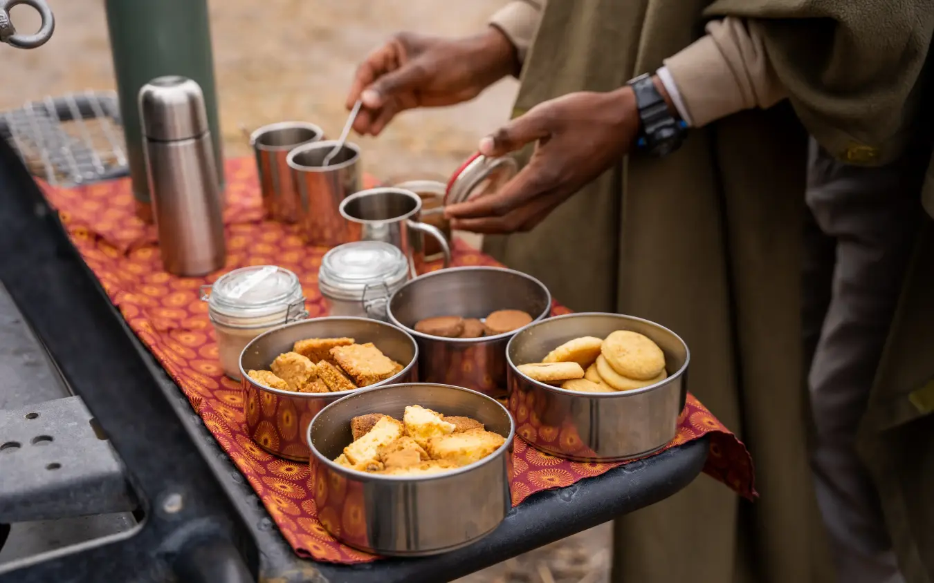 Safari guide serving food from metal containers on patterned cloth, Kwando Splash Camp, The Okavango Delta, Botswana