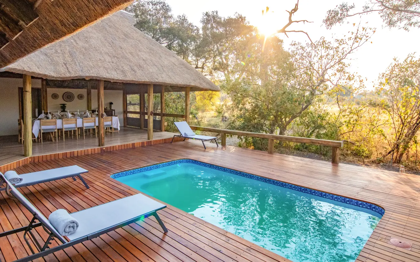Private pool deck with dining pavilion overlooking woodland landscape at sunset, Kwando Splash Camp, The Okavango Delta, Botswana