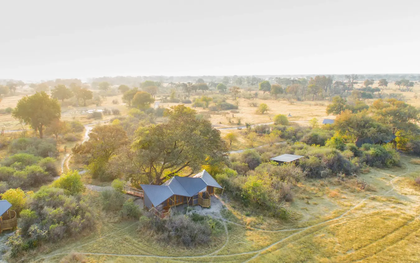 Luxury lodge with blue roof nestled among trees in expansive savanna landscape, Kwando Splash Camp, The Okavango Delta, Botswana