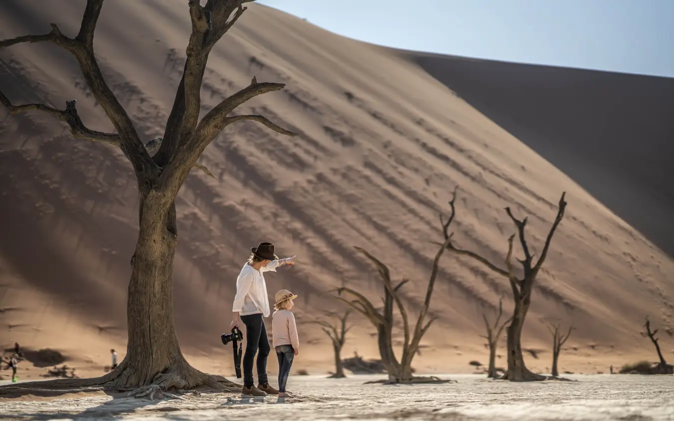 Adult and child standing beside dead tree in desert dune landscape, Kwessi Dunes, NamibRand Private Reserve, Namibia