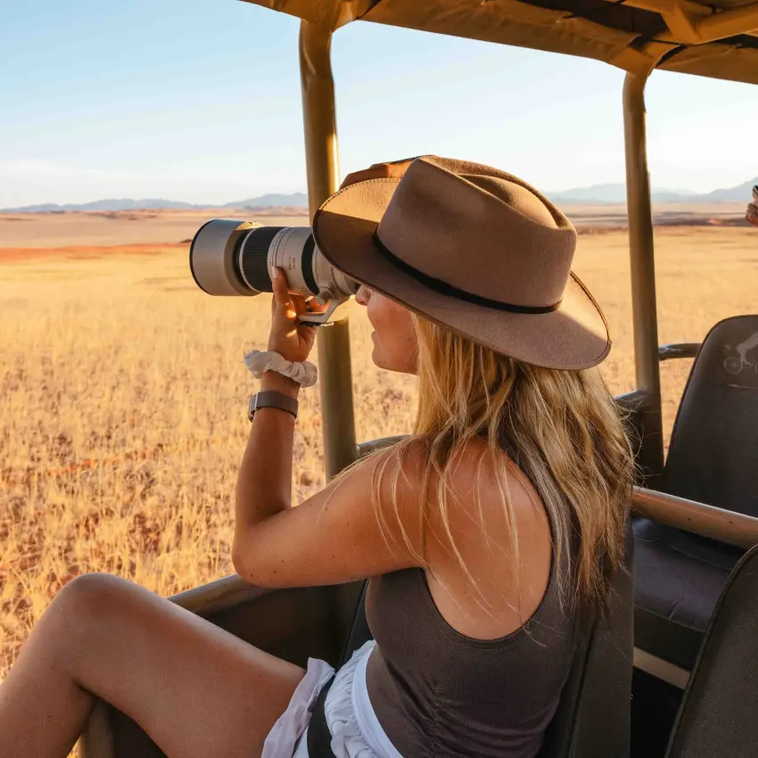 Woman photographing wildlife from safari vehicle in savanna grassland, Kwessi Dunes, NamibRand Private Reserve, Namibia