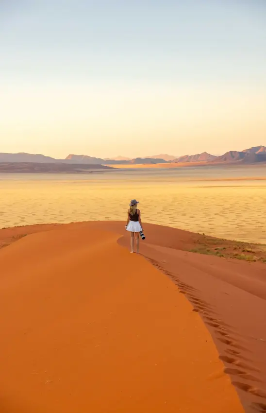 Solo traveler standing on red sand dune overlooking vast desert valley at sunset, Kwessi Dunes, NamibRand Private Reserve, Namibia