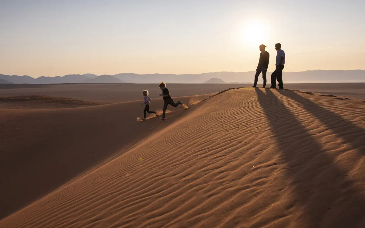 Family walking on sand dune at sunset with mountains in distance, Kwessi Dunes, NamibRand Private Reserve, Namibia