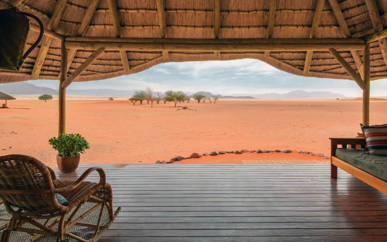 Thatched lodge veranda overlooking red desert landscape with acacia trees, Kwessi Dunes, NamibRand Private Reserve, Namibia