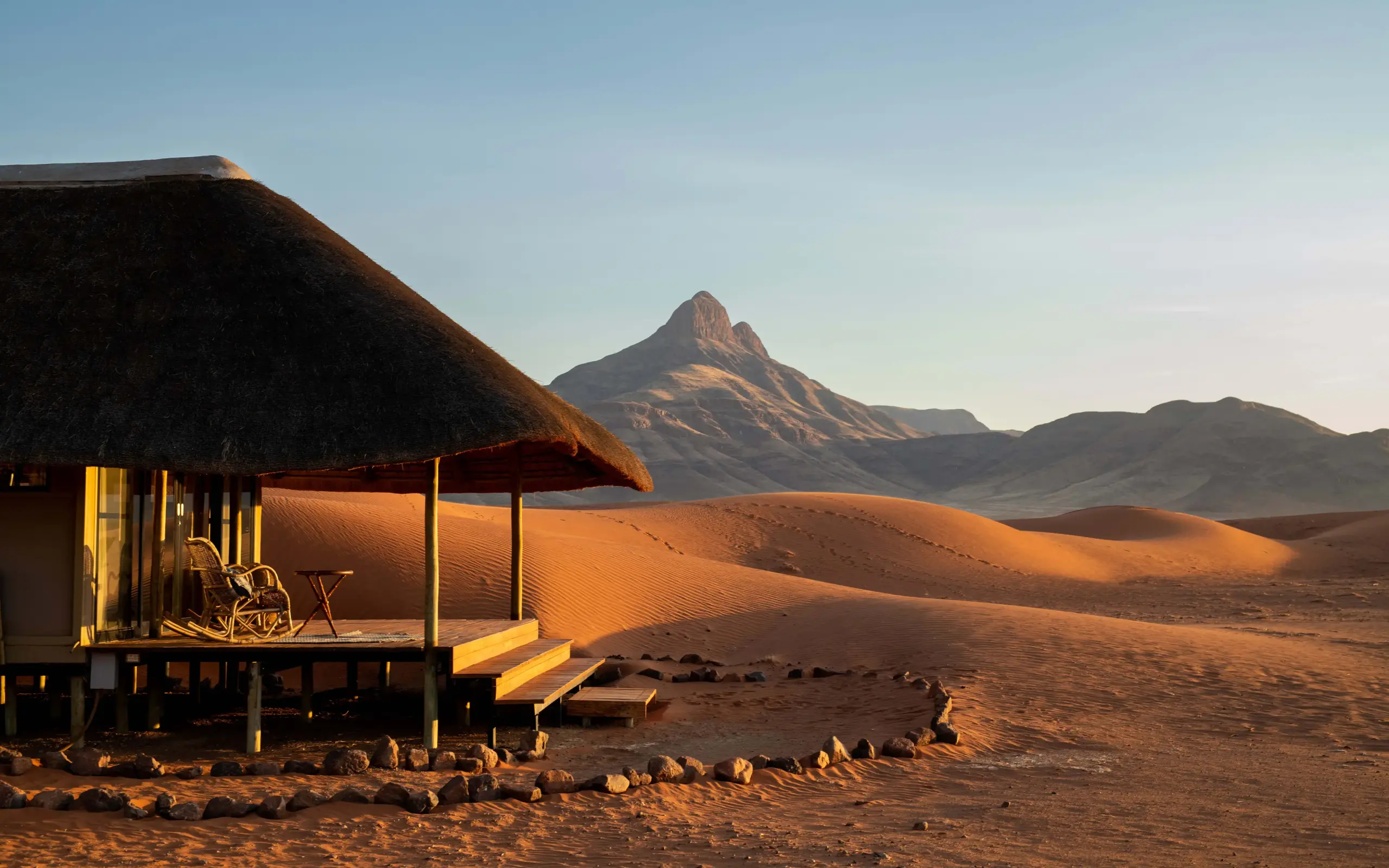 Thatched lodge with viewing deck overlooking desert dunes and mountain peak, Kwessi Dunes, NamibRand Private Reserve, Namibia