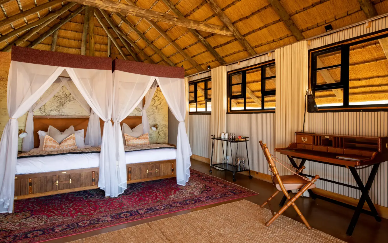 Luxury safari lodge bedroom with twin canopy beds and wooden beamed ceiling, Kwessi Dunes, NamibRand Private Reserve, Namibia