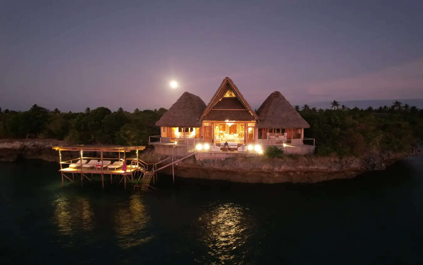Waterfront lodge with thatched roof structures illuminated at dusk with moon rising, Laba Fanjove, Zanzibar & Pemba, Tanzania