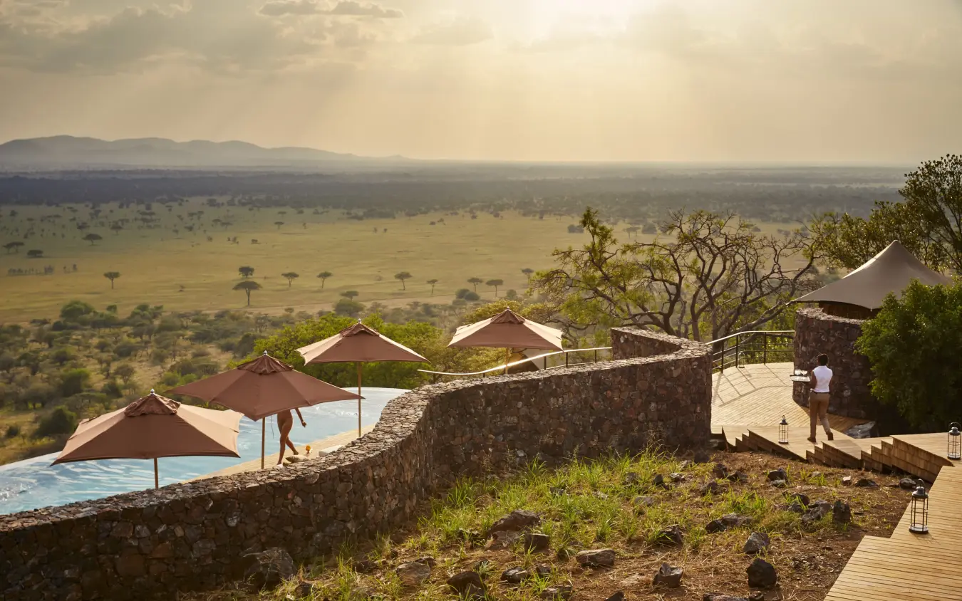 Infinity pool with sun umbrellas overlooking vast savanna plains and distant mountains, Laba Grumeti Art Lodge, Serengeti National Park, Tanzania