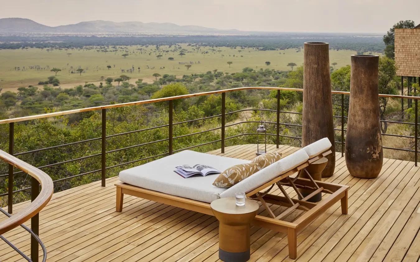 Spa bed on wooden deck overlooking vast savanna grassland with mountains, Laba Grumeti Art Lodge, Serengeti National Park, Tanzania