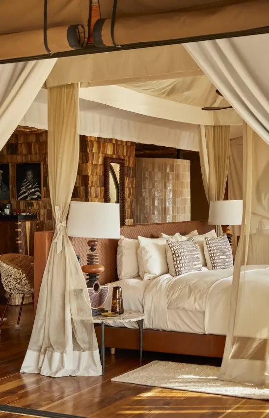 Luxury canopy bed in safari lodge bedroom with cream drapes and wooden accents, Laba Grumeti Art Lodge, Serengeti National Park, Tanzania