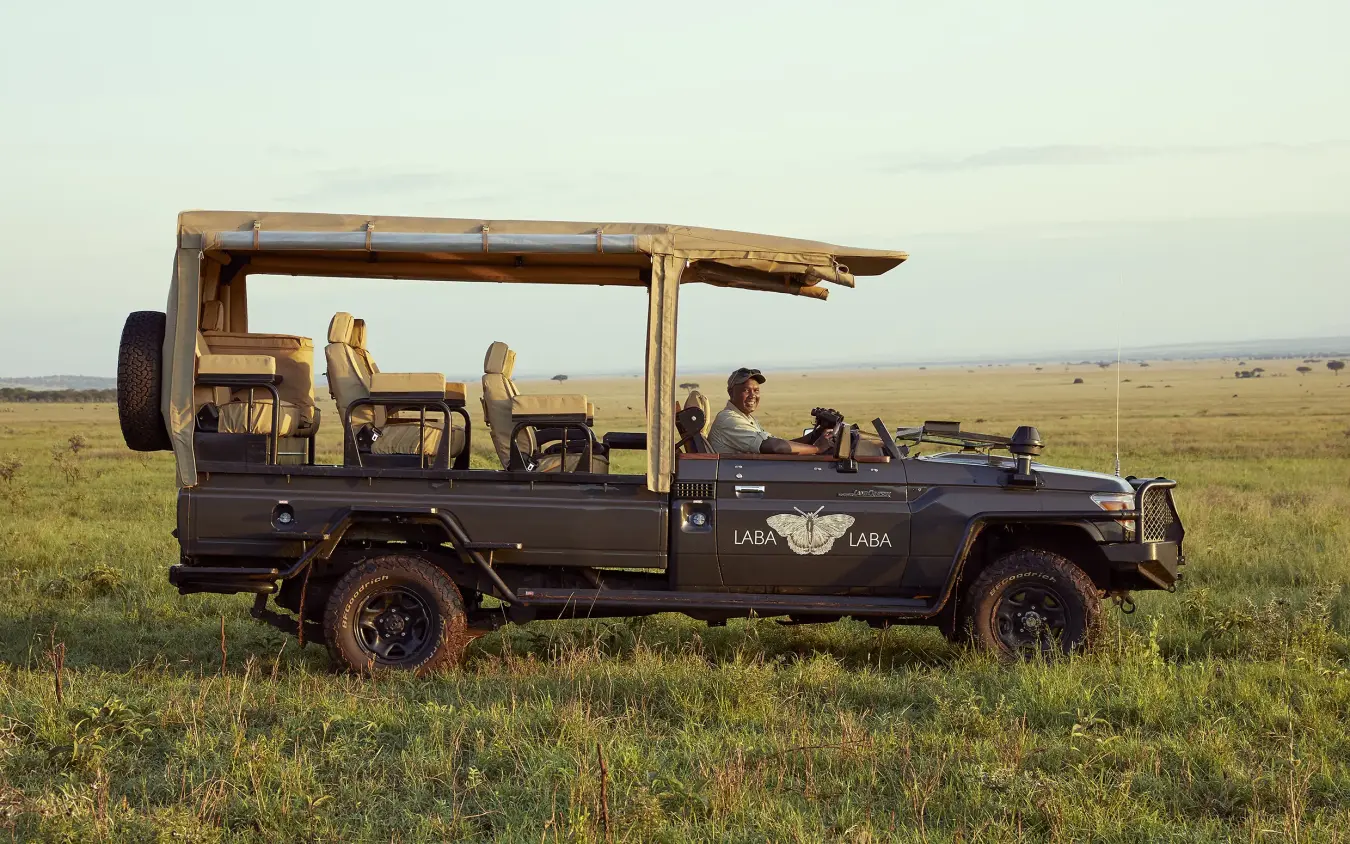 Open-sided safari vehicle with guests on game drive across grassland savanna, Laba Migration Camp, Serengeti National Park, Tanzania