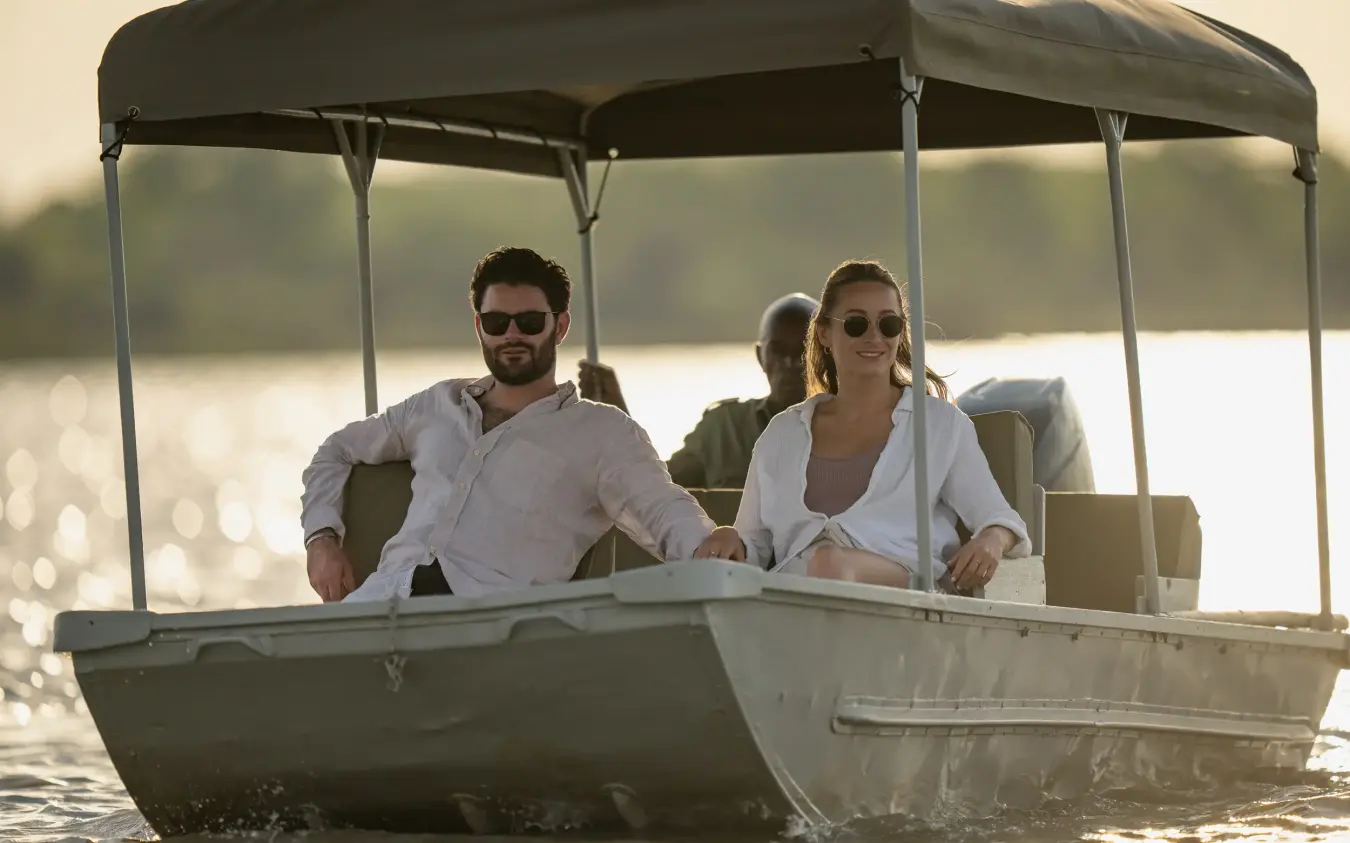 Couple on boat tour with canopy roof on calm waterway at sunset, Laba Siwandu, Nyerere National Park, Tanzania