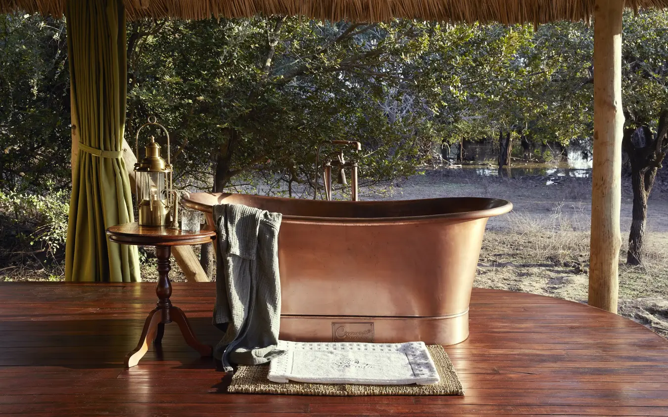 Outdoor bathroom with copper bathtub on wooden deck overlooking woodland savanna, Laba Siwandu, Nyerere National Park, Tanzania