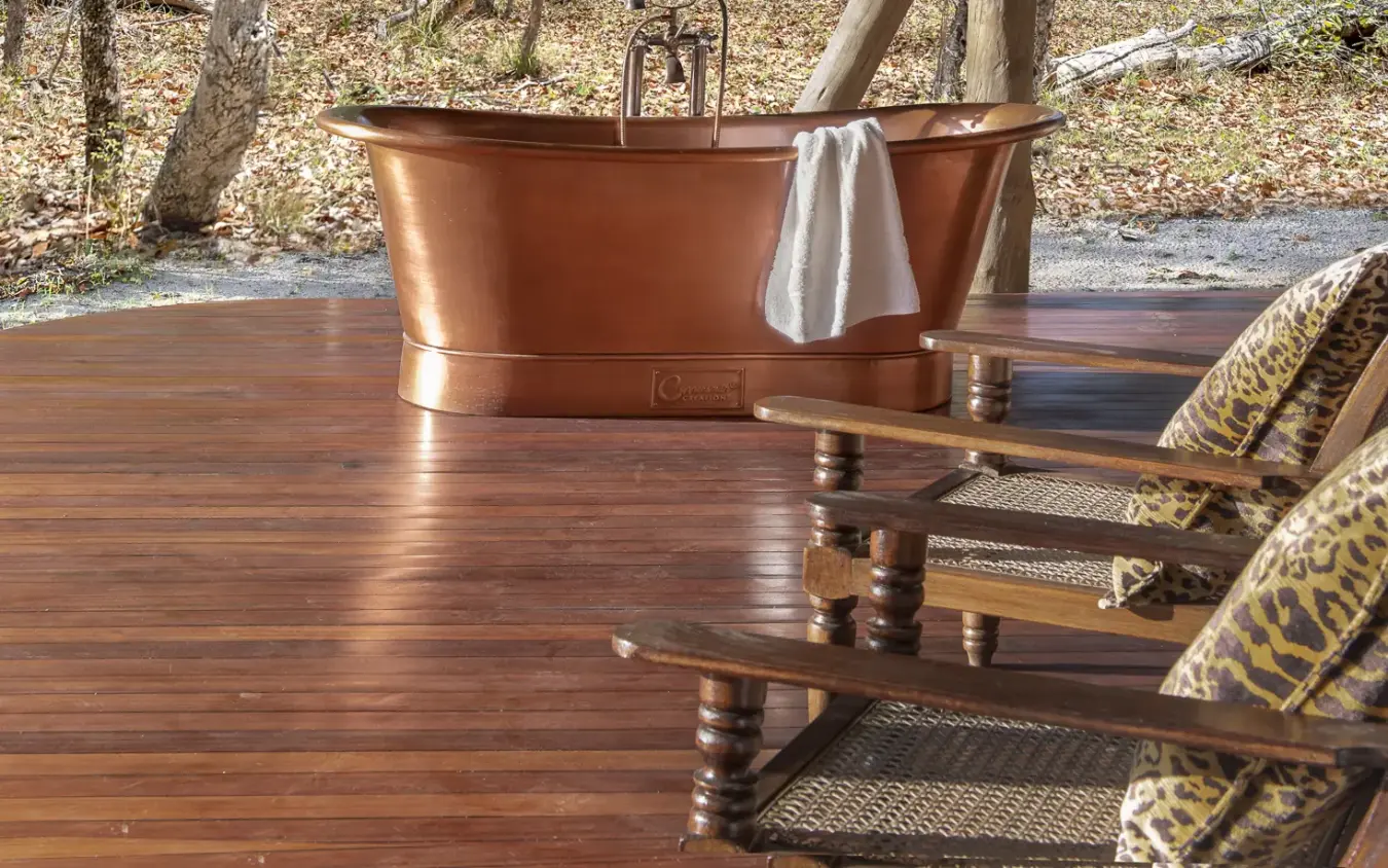 Copper soaking tub on wooden deck with forest backdrop and lounge chairs, Laba Siwandu, Nyerere National Park, Tanzania