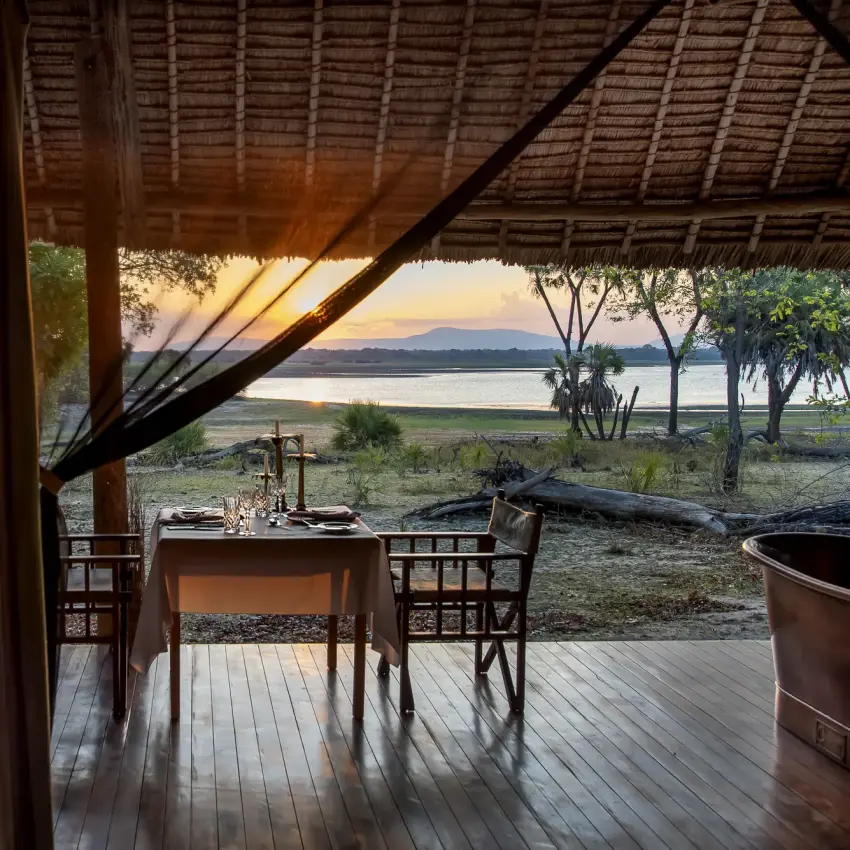 Dining table set for two on open-air deck overlooking waterside landscape at dusk, Laba Siwandu, Nyerere National Park, Tanzania