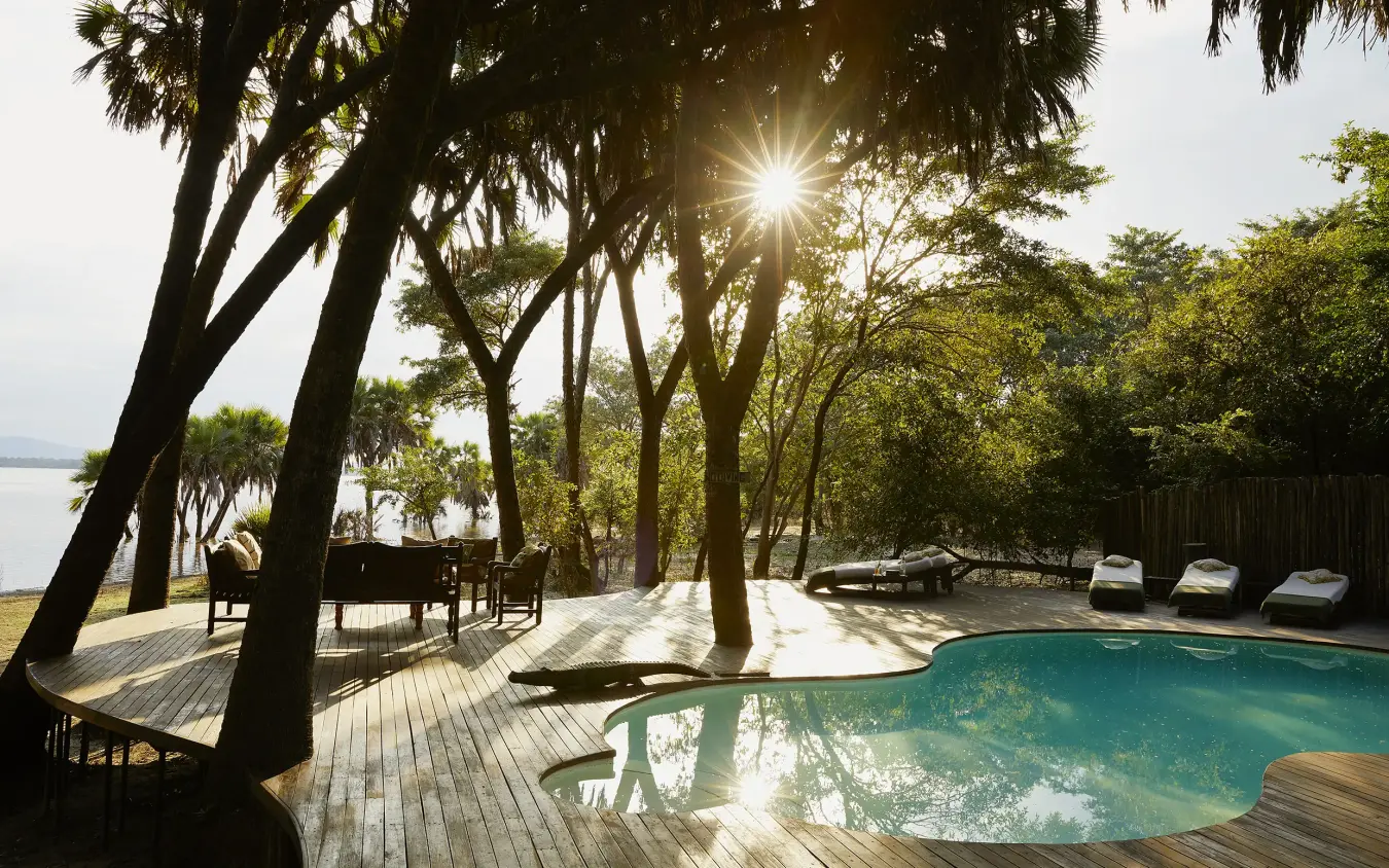 Waterfront pool deck with palm trees and wooden lounge chairs overlooking lake, Laba Siwandu, Nyerere National Park, Tanzania